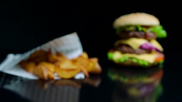 Francouzské hranolky a burger s dvojitým sýrem a čerstvou zelení na černém pozadí — Stock video