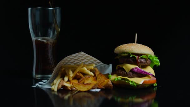 Налить стакан кока-колы и вкусный бургер, картофель фри на черном фоне для рекламы — стоковое видео