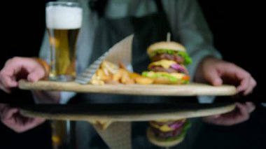 Şef dizi lezzetli hamburger, patates kızartması, bira siyah arka plan üzerine ahşap tepsi üzerinde hizmet veren