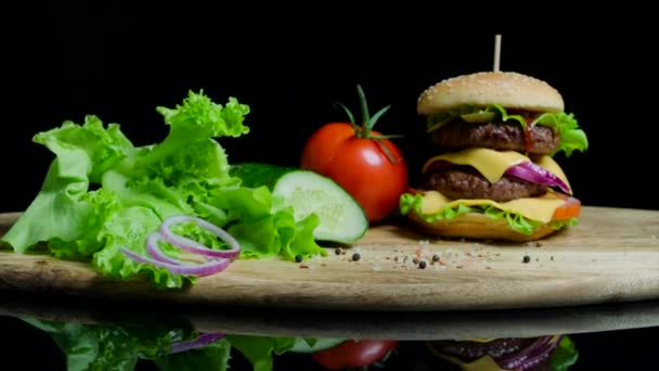 Fresh vegetables and tasty burger with cheese and beef cutlets on the black background — Stock Video