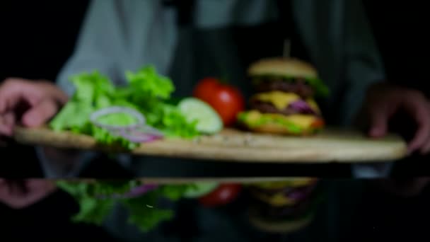 Verduras frescas y sabrosa hamburguesa con queso y chuletas de ternera. Chef en el fondo fuera de foco — Vídeos de Stock