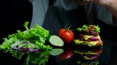 Sığır eti, peynir ve sebze ile lezzetli burger bitirme Şef. Ticari için siyah arka plan