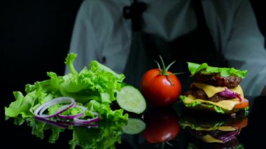 Sığır eti, peynir ve sebze ile lezzetli burger bitirme Şef. Ticari için siyah arka plan