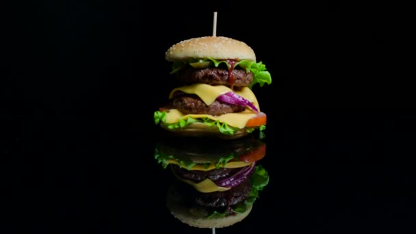 Sabrosa hamburguesa con carne de res, queso y verduras en el fondo de cristal negro para comercial — Vídeo de stock