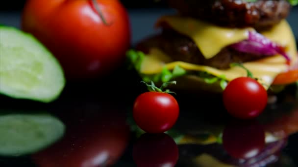 Közelkép a friss zöldségek és finom hamburgert, a sajt és a marhahús szelet a fekete háttér — Stock videók