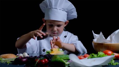 Küçük çocuk mutfağa bir burger yemek, şefler takım elbise