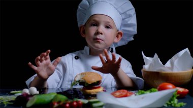 Sevimli çocuk Ingredientes siyah arka plan üzerine yemek ile çevrili şefler takım elbise giyiyor