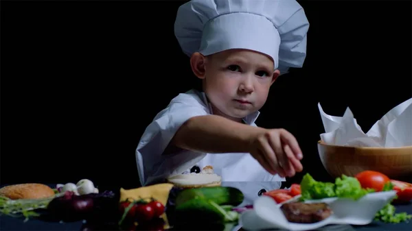 Le petit garçon cuisine à la cuisine, il porte un costume de chef — Photo