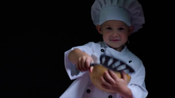Garoto sorridente vestindo terno de chefs com tigela de batatas fritas no fundo preto — Vídeo de Stock