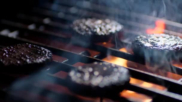 Primer plano de las chuletas de hamburguesas en la parrilla con llamas de fuego, chef los da la vuelta, cámara lenta — Vídeo de stock
