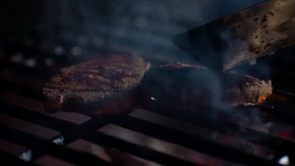 Close up of steaks on grill with fire flames, chef turns them over, slow motion — Stock Video