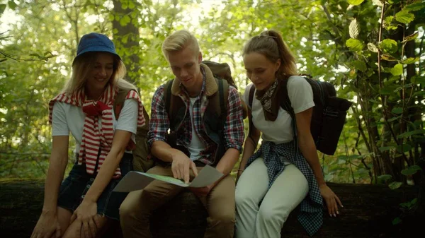 Mochileros aprendiendo el mapa del viajero sentados en un árbol caído en el bosque — Foto de Stock