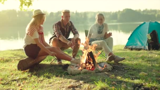 Bästa vänner matlagning marshmallows på binfire på vandring nära sjön på sommarlovet. Camping i bakgrunden — Stockvideo