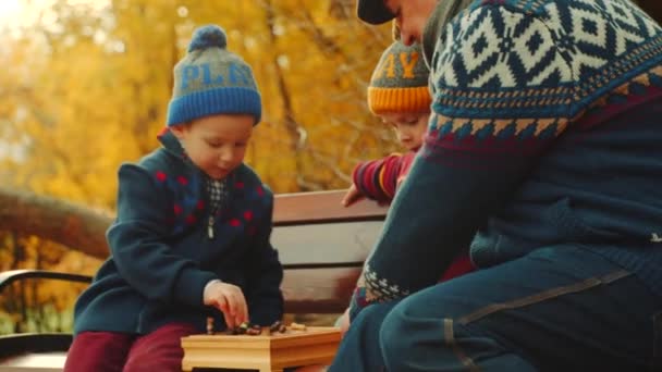 Vnuci hrají šachy s dědou na lavičce v podzimním parku — Stock video
