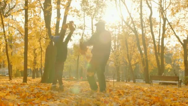 Dědeček a vnuk jsou vyhazování spadané listí a hraje v podzimní park — Stock video
