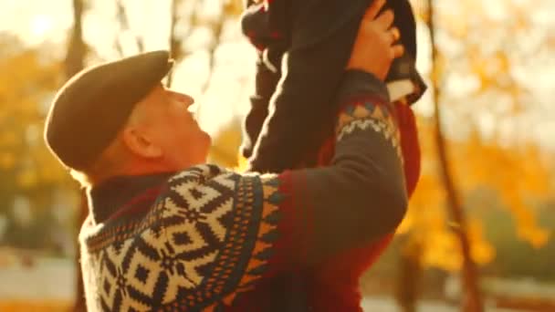 Abuelo lanzando a su nieto en los brazos en el parque de otoño — Vídeos de Stock