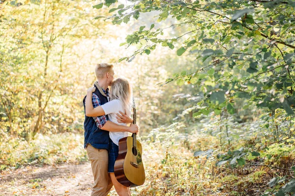 Romántica pareja joven abrazándose en el parque en verano con la guitarra en las manos —  Fotos de Stock