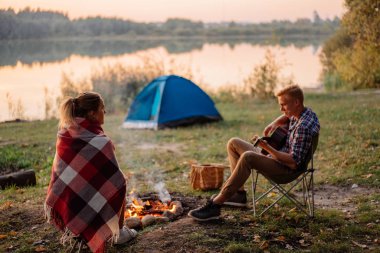 Genç adam gitar şenlik ateşi yakın arkadaşına günbatımında zammı üzerinde oynama