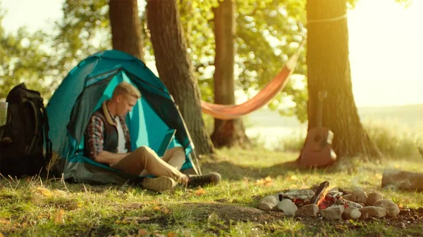 Young man working at laptop during camping with tents at sunset