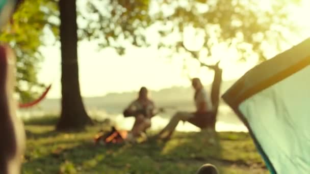 Giovane uomo sta aprendo tenda e raggiungendo i suoi amici al falò con la chitarra in campeggio mangiare tramonto — Video Stock