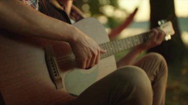 Genç adam günbatımında kamp alanında gitar çalmak