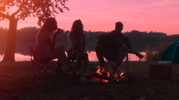 Venner nyder solnedgang nær bål på campingpladsen på vandreture – Stock-video