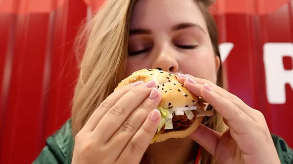 Mujer joven disfrutando de deliciosa hamburguesa con los ojos cerrados —  Fotos de Stock