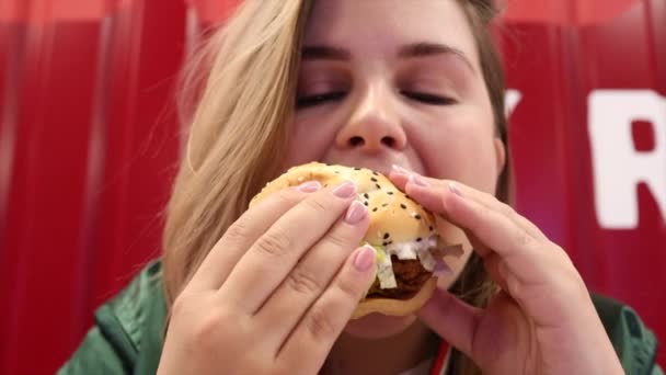 Mladá žena se těší vynikající burger s očima uzavřena v rychlé občerstvení café — Stock video
