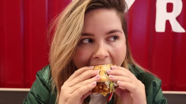 Feliz joven comiendo deliciosa hamburguesa y sonriendo — Vídeo de stock