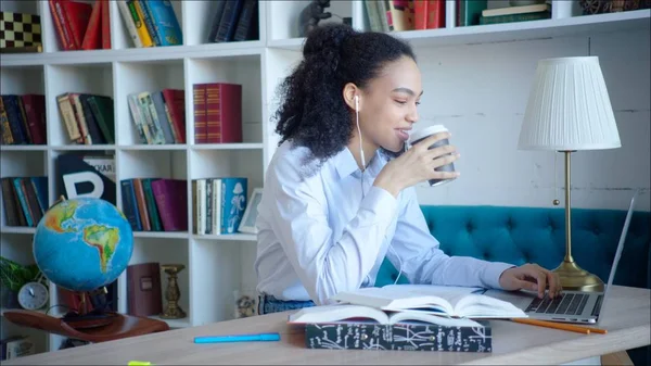 Giovane donna sta leggendo per gli esami nella biblioteca del campus all'università. Giovane studente afroamericano sta bevendo caffè durante la lettura di articoli nel computer — Foto Stock