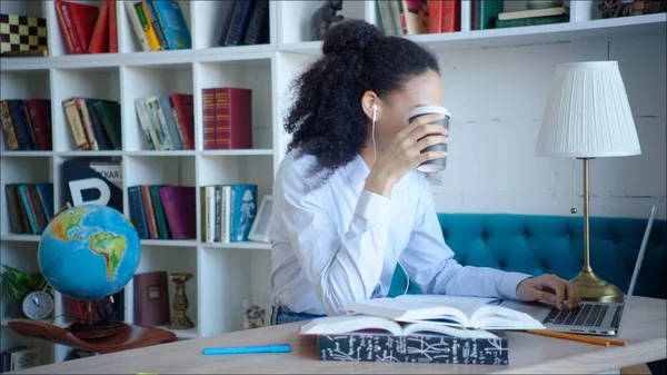 No face African american female student reading up for examination at the library using laptop with coffee cup in her hand. It overlaps her face