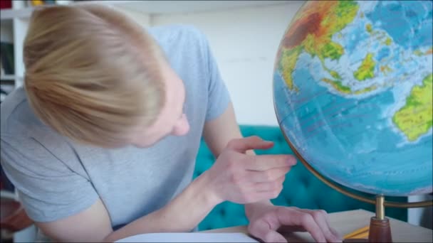 Young blonde man spinning the globe and looking for the island in the pacific ocean — Stock Video