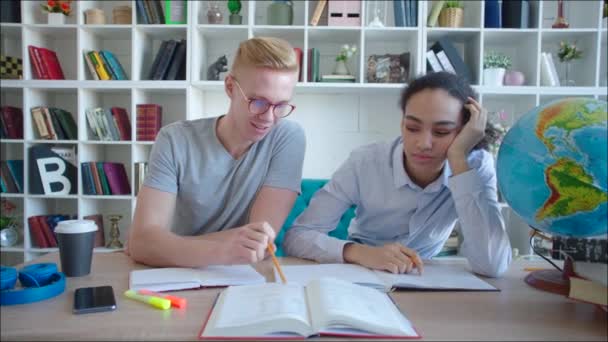Manlig student att hjälpa afrikanska kaukasiska kvinnliga elev läsa för examen i biblioteket — Stockvideo