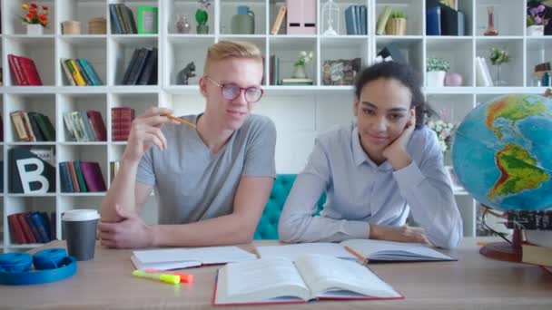 Portret van twee gelukkige Afrikaanse en Kaukasische studenten voorbereiden op examen samen in de Universiteitsbibliotheek — Stockvideo