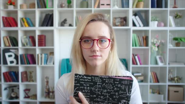 Retrato femenino serio de estudiante con gafas y con libro de texto en las manos en la universidad — Vídeo de stock