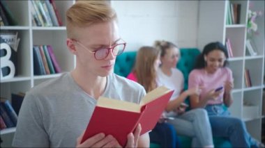 Genç kızlar değişim sırasında onun arkasına gülüyor iken erkek nerd öğretici okuyor