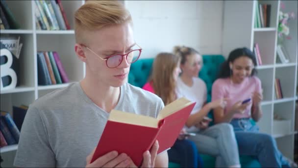 Masculino nerd está lendo tutorial enquanto teen meninas estão rindo atrás dele de volta durante mudança — Vídeo de Stock