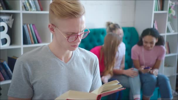 Geek está lendo tutorial enquanto as meninas adolescentes estão rindo atrás de suas costas — Vídeo de Stock