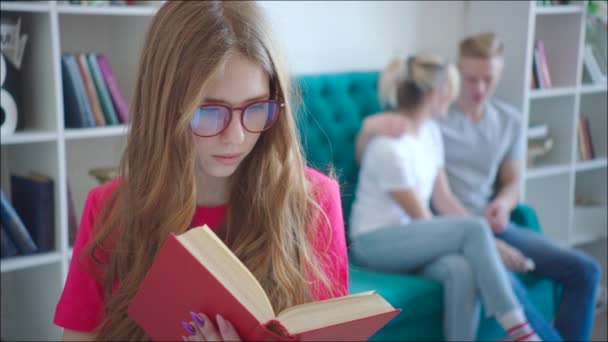Vrouwelijke Geek is het lezen van de tutorial terwijl paar knuffelen op de Bank in de bibliotheek — Stockvideo