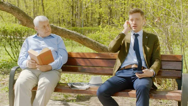 Yaşlı adam th parkta kitap okuyor ve işadamı ses kulaklık ile telefonda yüksek sesle konuşma ile rahatsız ediyor