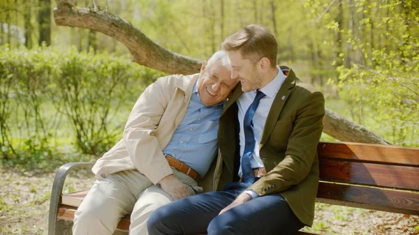 Youn man is hugging his old father on the bench in the autumn park