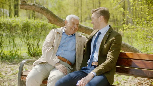 Young man is smiling to his senior farher on meeting in the park on summer day