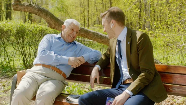 Viejo y joven están teniendo una charla en el banco en el parque Fotos De Stock