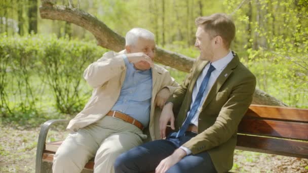 Youn man is hugging his old father on the bench in the autumn park — 비디오