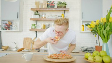 Sarışın adam mutfakta kahvaltı yaparken pizza yiyor