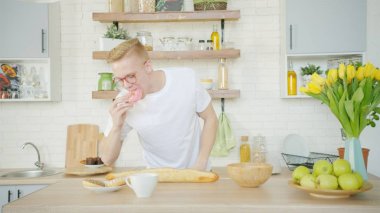 Sarışın adam mutfakta kahvaltı için çörek yiyor