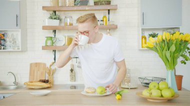 Sarışın adam mutfakta kahvaltı yaparken kahve içiyor