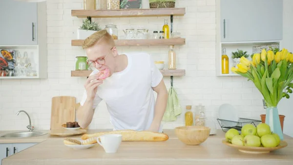 Szőke ember eszik fánk reggelire a konyhában Stock Fotó