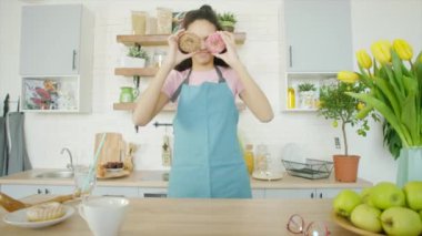 Genç kadın elinde çöreklerle mutfakta aylaklık ediyor.