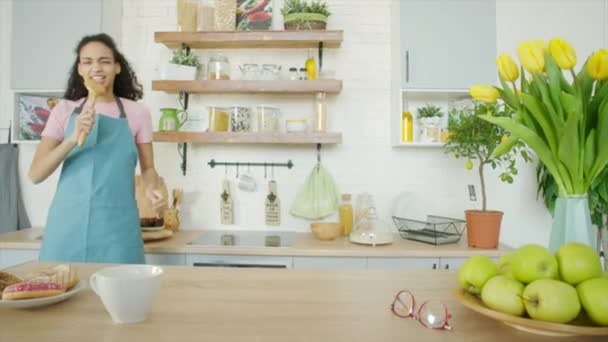 Wanita muda bermain-main dan bernyanyi dengan roti bukannya mikrofon di dapur — Stok Video